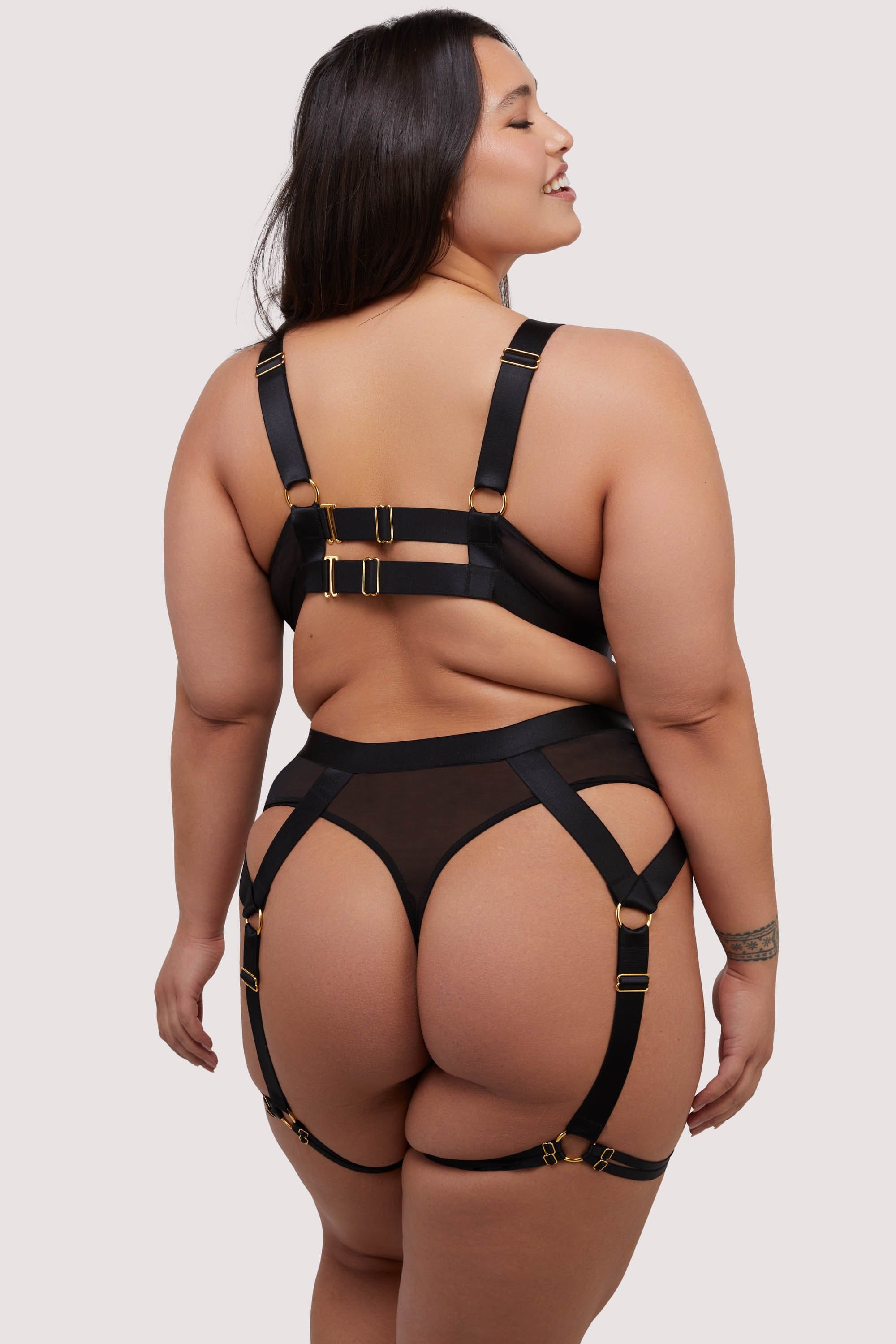 model shows the back of the black mesh elastic multi strap bodysuit