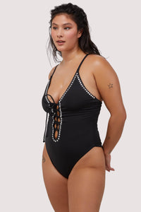 Model wears black plunge neckline lace-up swimsuit with silver studs