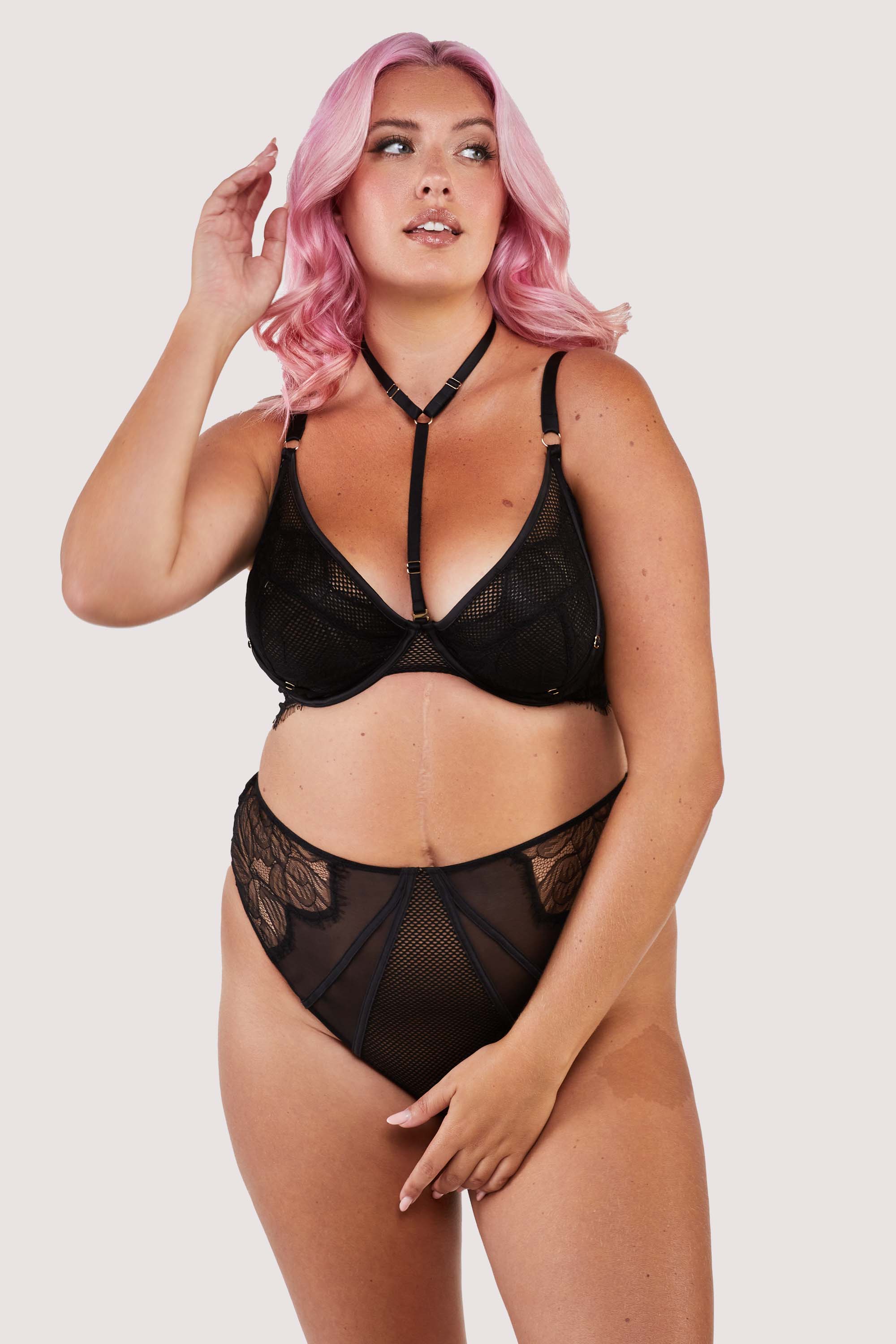 Black lacy fishnet plunge bra with gold hardware, worn with a matching brief.