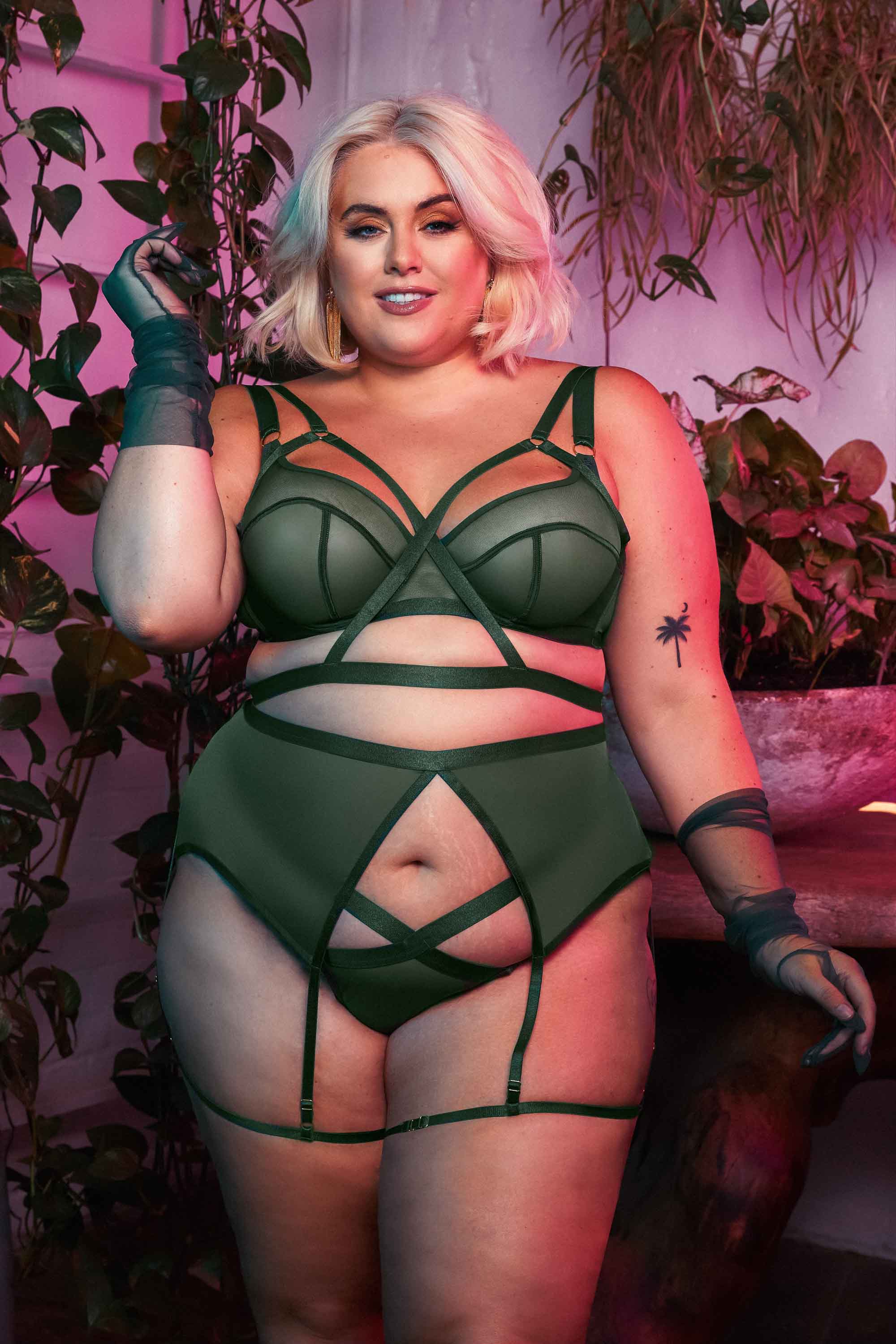 Green satin harness style bra seen with matching brief and suspender.