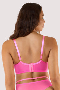 Model shows back of neon pink balconette bra with strappy details and sheer mesh panels, showcasing a bold design.