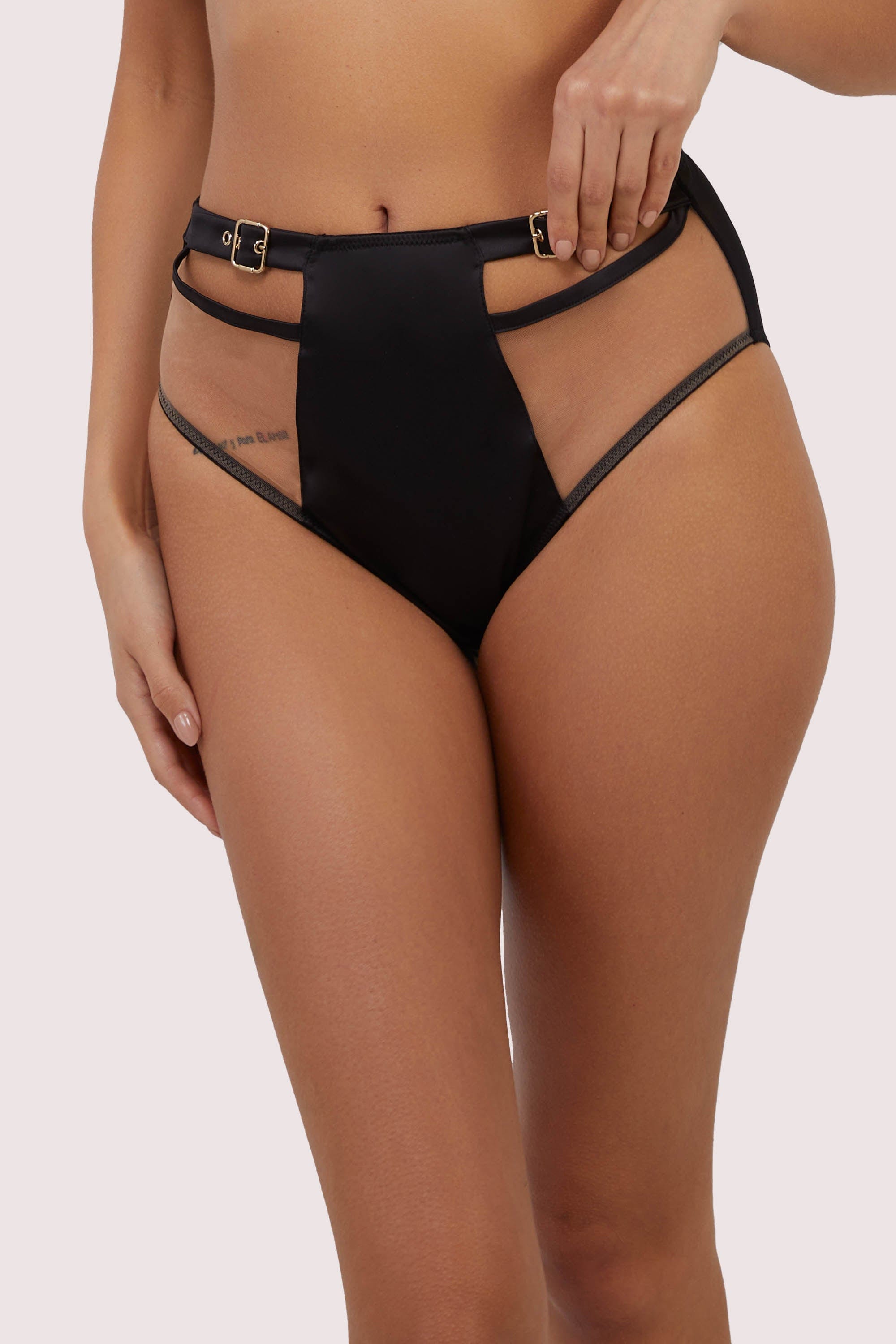 Model wears black satin and mesh high-waist briefs with gold buckles