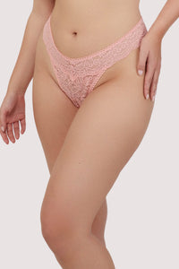 Model wears coral lace thong with high-rise fit and scalloped lace waistband