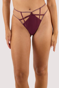 Model wears a wine high waist thong featuring a satin central panel, strap detailing, and gold metal hardware.