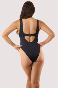 Model Back view in a black textured one-piece swimsuit with a square neckline and gold buckle belt, showcasing a sleek silhouette.