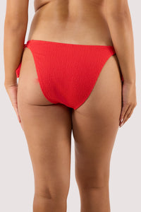 Model Back view of red textured bikini bottoms in a cheeky cut, worn by a woman, showing the snug fit and ribbed fabric detail.