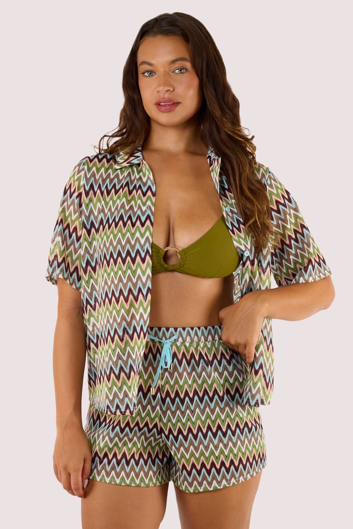 Model Wearing khaki bikini top and shorts, complemented by a breezy crochet beach shirt with a button-down front and zig-zag pattern.