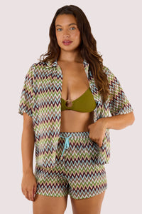 Model Wearing khaki bikini top and shorts, complemented by a breezy crochet beach shirt with a button-down front and zig-zag pattern.