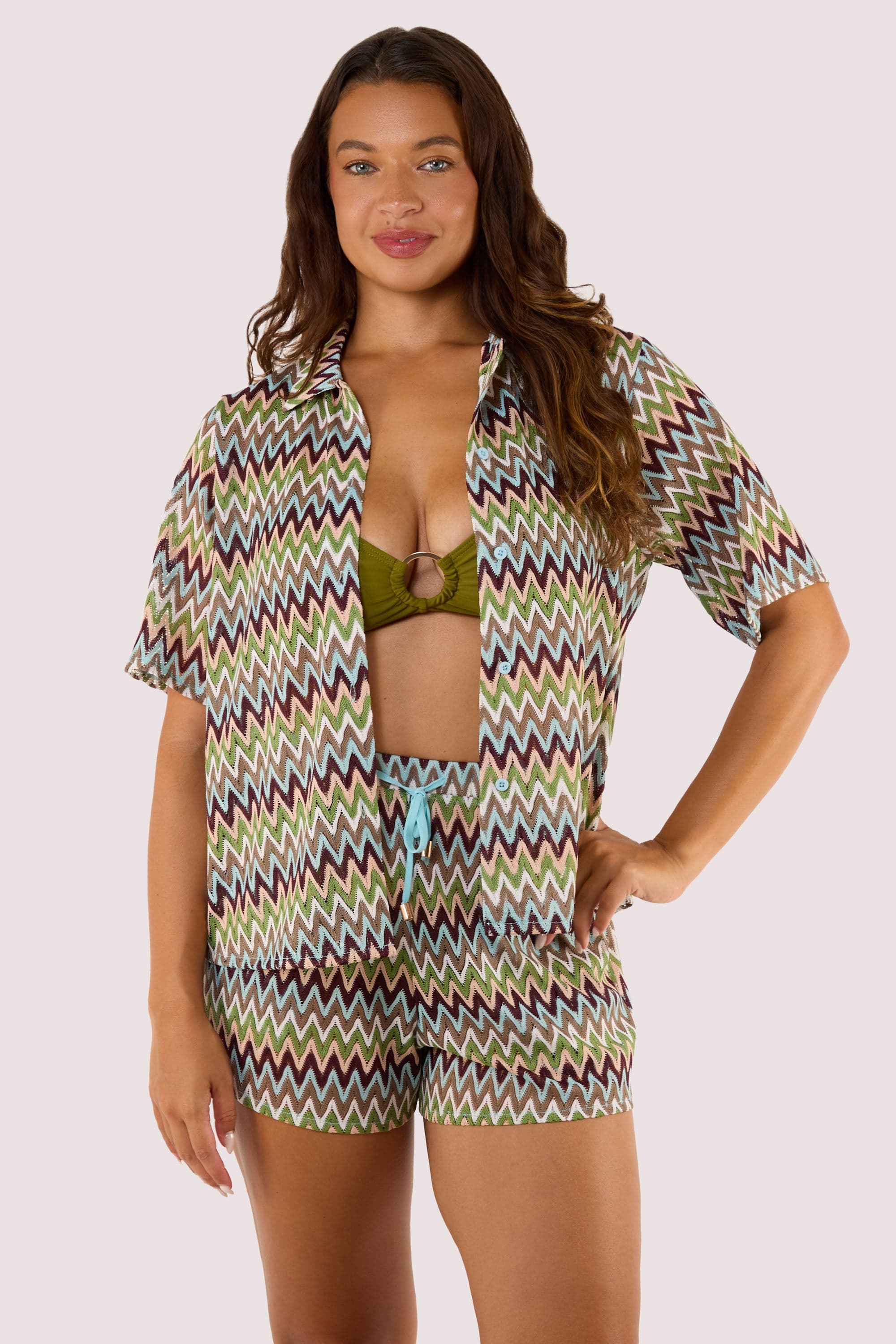 Model wearing a short-sleeved, button-down crochet beach shirt with a zig-zag pattern and relaxed fit, paired with shorts.