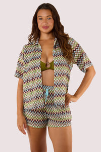 Model wearing a short-sleeved, button-down crochet beach shirt with a zig-zag pattern and relaxed fit, paired with shorts.