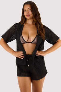 Model Wearing a black swimsuit stands confidently with hands on hips, wearing a lightweight black crochet beach shirt.