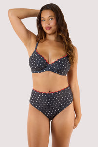 model Waering a black polka dot bikini top with red scalloped edges, designed for fuller busts with adjustable straps and support.
