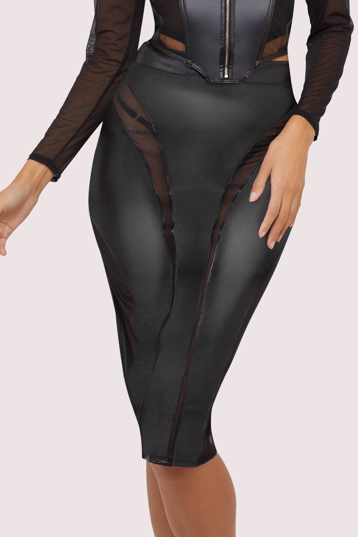 Model wears a black vegan leather mesh insert pencil skirt featuring leather panels with sheer mesh inserts with waist cinching, silhouette defining fit.