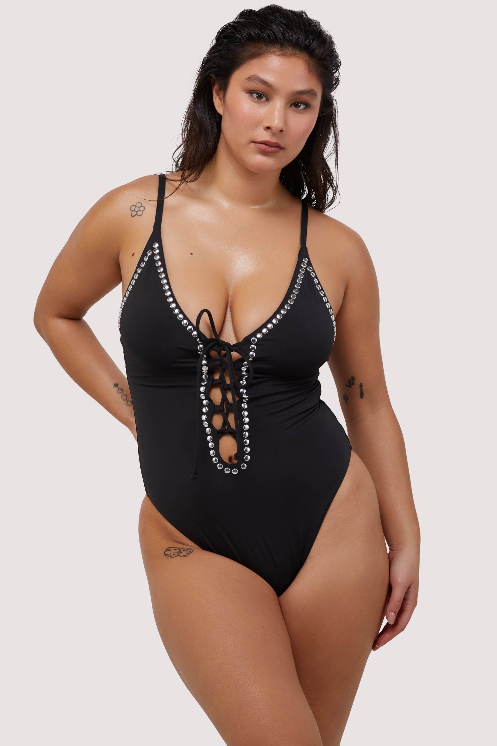 Model wears black plunge neckline lace-up swimsuit with silver studs