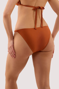 Model shows the back of a georgia brown high shine tie side bikini brief with hardwear.